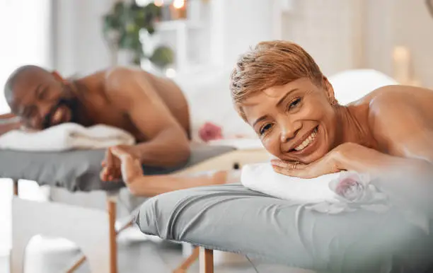 Love, massage and couple holding hands at a spa in celebration of a happy marriage anniversary holiday. Smile, romance and relaxed black woman with a happy romantic African partner at a luxury resort
